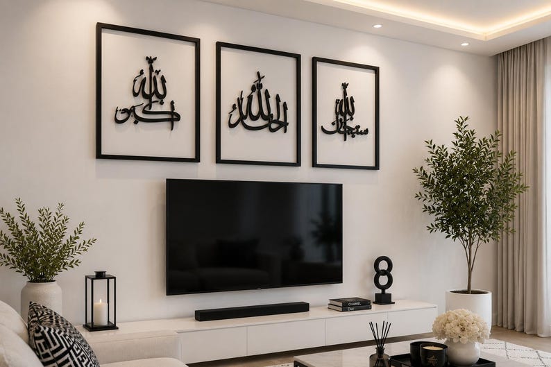 May include: Three framed black wall art pieces with Arabic calligraphy hang above a large flat-screen TV. The room features a white entertainment center, a decorative plant, and a modern aesthetic.