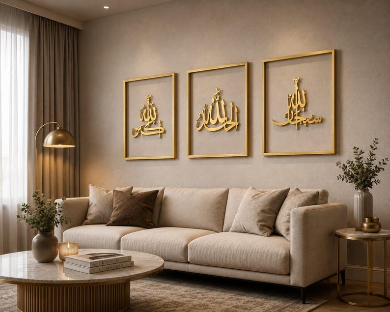May include: Three framed gold-colored Islamic calligraphy art pieces hang above a beige sofa. The artwork features ornate Arabic script within gold frames. The room has a neutral color palette with a gold floor lamp and a marble coffee table.