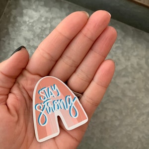 May include: A pink and white rainbow-shaped sticker with the text "Stay Strong" in blue lettering.