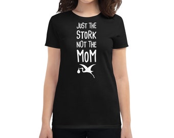 May include: Black women's t-shirt with white text that reads "Just the Stork not the Mom" and a white silhouette of a stork carrying a baby.