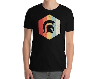 Puede incluir: Una camiseta negra con un gráfico retro de un casco espartano en forma de hexágono. El gráfico tiene un aspecto descolorido y vintage con colores rojo, naranja, amarillo, azul y verde.