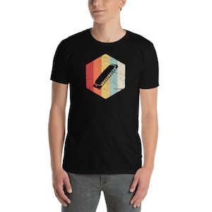 May include: A black t-shirt with a vintage-style graphic of a harmonica in a hexagon. The graphic has a faded, retro look with red, orange, yellow, blue, and green colors.