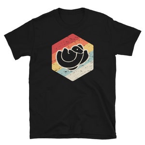 Puede incluir: Una camiseta negra con un gráfico retro de un pájaro enroscado en un hexágono. El hexágono tiene un esquema de color rojo, naranja, amarillo y azul.