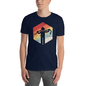 Könnte beinhalten: Ein marineblaues T-Shirt mit einer Retro-Grafik einer Person, die eine Schlange hält. Die Grafik ist in einer sechseckigen Form mit einem verblassten Regenbogen-Farbschema.