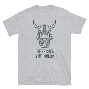 Puede incluir: Camiseta gris con un dibujo lineal de un vikingo con un casco con cuernos. El texto "Leif Erikson is my homeboy" está impreso debajo de la imagen.