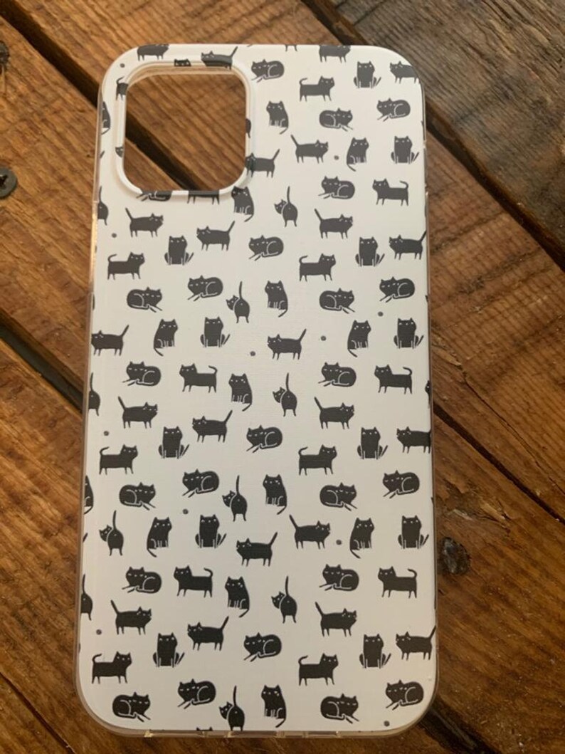 May include: A white phone case with a black cat pattern. The case has a cutout for the camera lens.