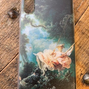 Puede incluir: Una funda de tel&eacute;fono con una pintura de una mujer en un columpio en un entorno de bosque. La mujer lleva un vestido rosa y un sombrero blanco. La pintura es de estilo cl&aacute;sico.