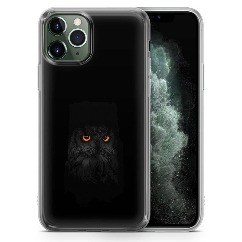 May include: A clear phone case with a black owl with orange eyes on the back. The owl is in the center of the case and is facing forward. The case is designed for an iPhone.