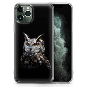 May include: A clear phone case with a black background and a detailed image of an owl with yellow eyes. The owl is facing the camera and has a dark brown and black patterned design.
