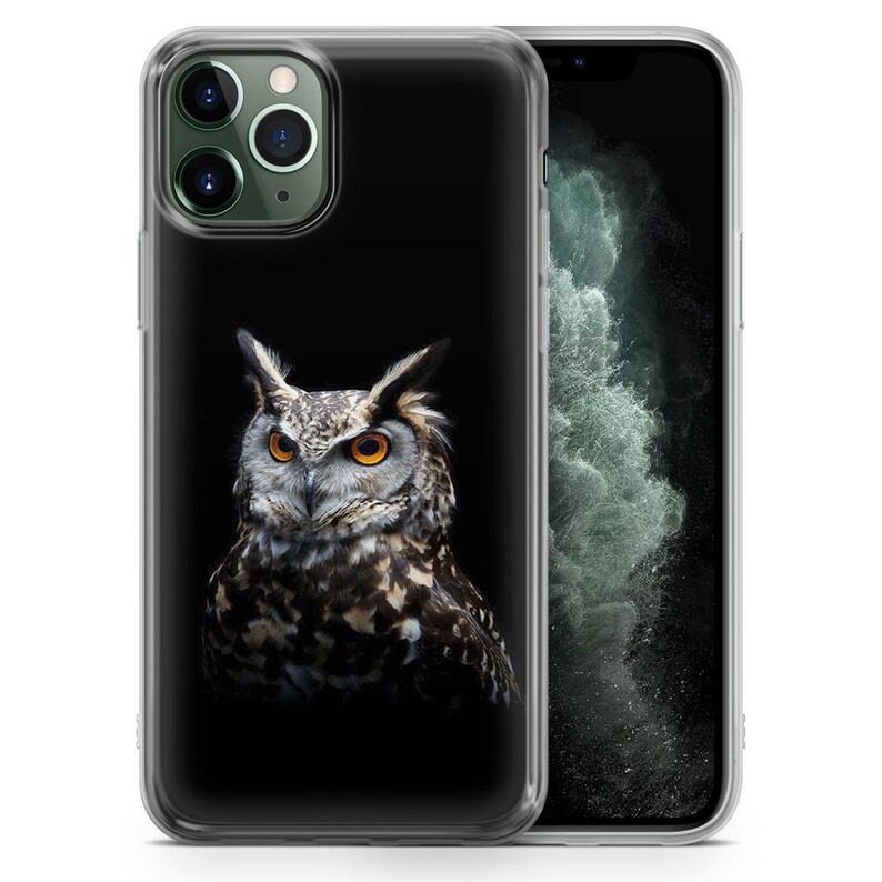 May include: A clear phone case with a black background and a detailed image of an owl with yellow eyes. The owl is facing the camera and has a dark brown and black patterned design.