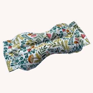 May include: A white fabric eye mask with a pattern of green leaves, red and yellow mushrooms, and white dots.