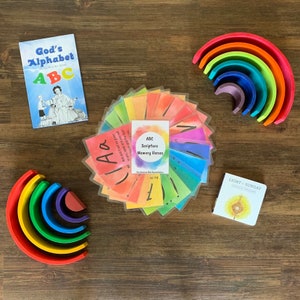 Puede incluir: Un conjunto de tarjetas de alfabeto coloridas con versículos de la Biblia. Las tarjetas están dispuestas en círculo y tienen un fondo de acuarela. Las tarjetas están etiquetadas con las letras del alfabeto y un versículo bíblico correspondiente. Las tarjetas forman parte de un conjunto de materiales educativos para niños.