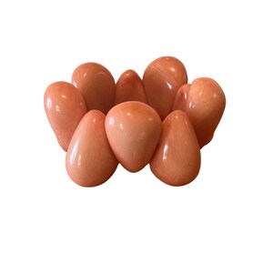 May include: A coral-colored bracelet made of smooth, rounded stones. The bracelet is made up of eight stones, each with a slightly different shape and size.