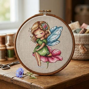 May include: A cross-stitch embroidery in a wooden hoop features a fairy with blonde hair, a green dress, and blue wings, seated on a pink flower. The artwork is set against a neutral fabric background, showcasing a whimsical, fantasy theme.