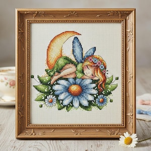 May include: Cross-stitch artwork of a sleeping fairy on a blue flower, framed in a decorative wooden frame. The fairy has red hair, a green dress, and blue wings. The artwork includes a crescent moon and small daisies.