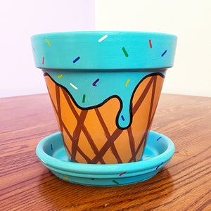 May include: A turquoise ceramic planter painted to look like an ice cream cone with brown waffle cone details and colorful sprinkles.