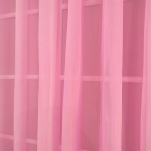May include: Pink sheer curtains hanging in a window. The curtains are made of a lightweight fabric and have a soft, flowing drape.
