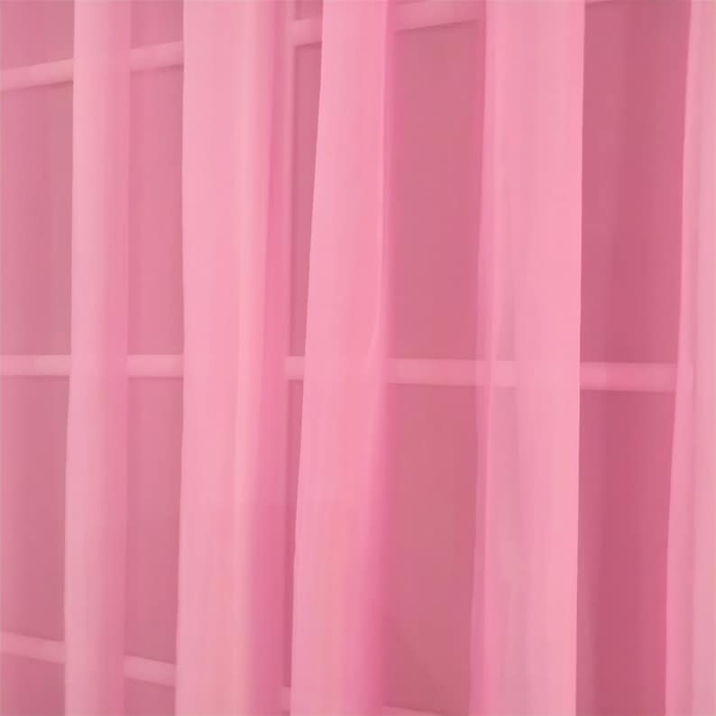 May include: Pink sheer curtains hanging in a window. The curtains are made of a lightweight fabric and have a soft, flowing drape.