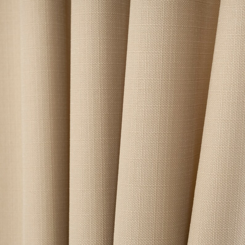 May include: Close-up of a beige fabric with a textured weave. The fabric is folded in a series of pleats, creating a soft and inviting look.