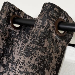 Puede incluir: Primer plano de dos cortinas con estampado negro y marrón con ojales en la parte superior, colgadas de una barra de cortina negra.