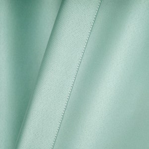 May include: A close-up of a light green fabric with a subtle texture and a straight seam running diagonally across the surface.