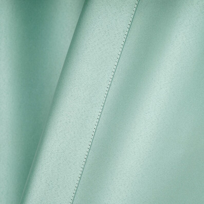 May include: A close-up of a light green fabric with a subtle texture and a straight seam running diagonally across the surface.