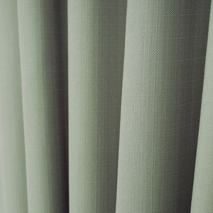 May include: Close-up of a set of green curtains with a textured woven fabric.