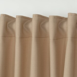 May include: Close-up of a set of beige curtains with a textured woven fabric. The curtains are gathered at the top and have a subtle sheen.