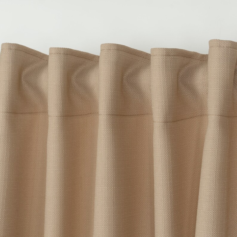 May include: Close-up of a set of beige curtains with a textured woven fabric. The curtains are gathered at the top and have a subtle sheen.