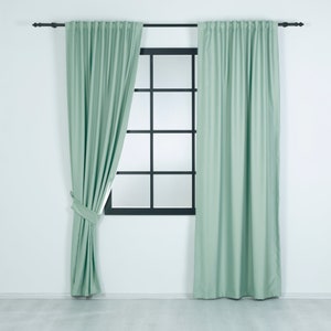 May include: A pair of light green curtains hanging on a window with a black frame. The curtains are drawn back on one side, revealing the window behind.