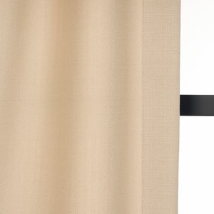 May include: A close-up of a beige curtain with a subtle textured weave. The curtain is hanging from a black rod.