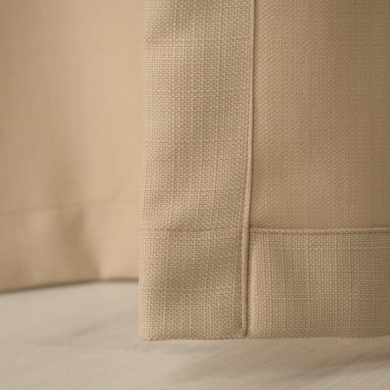 May include: Close-up of the bottom edge of a beige curtain panel. The fabric has a woven texture and a subtle sheen.