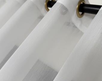 May include: White sheer curtains with silver grommets hanging on a black curtain rod.