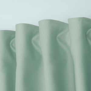 May include: Close-up of a set of three light green curtains with a subtle texture. The curtains are gathered at the top and have a simple, elegant design.