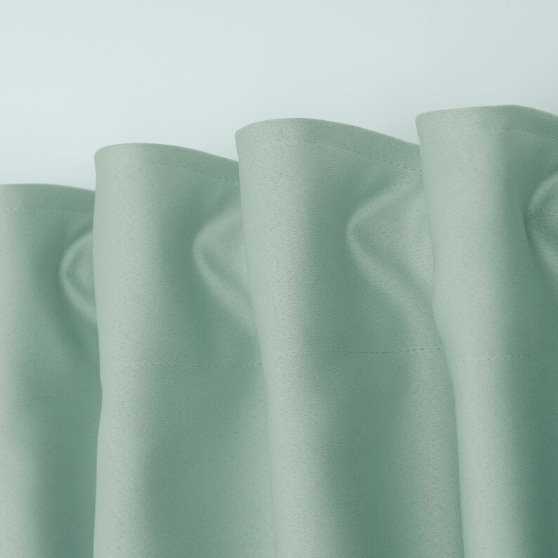 May include: Close-up of a set of three light green curtains with a subtle texture. The curtains are gathered at the top and have a simple, elegant design.