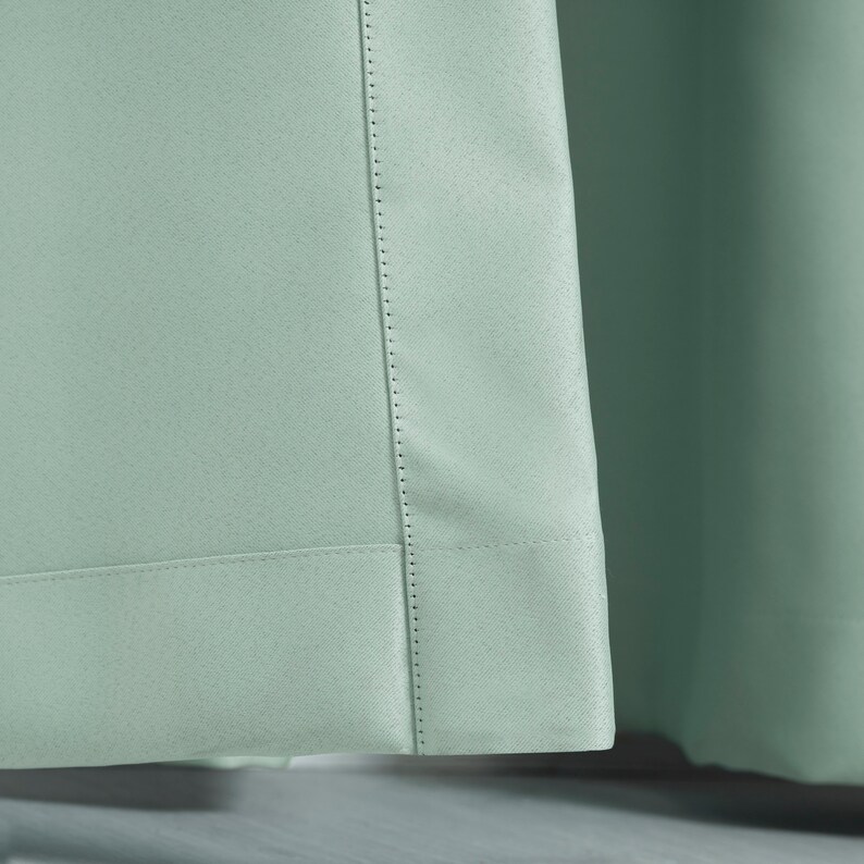 May include: Close-up of a light green curtain panel with a stitched hem and a decorative seam running down the side.