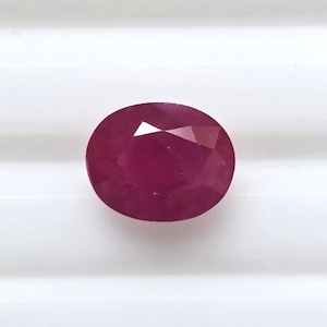 May include: Oval-shaped, faceted ruby gemstone. The gem is a deep, rich red color, with multiple facets that catch the light. The ruby is set against a white background, highlighting its color and shape. This gemstone is suitable for jewelry making.