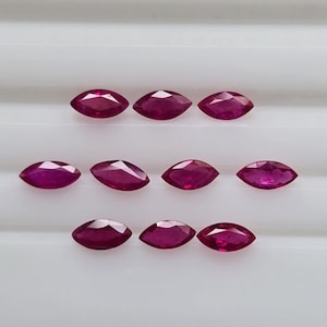 May include: Eleven marquise-cut rubies, each with a deep red colour, are displayed. The gemstones are arranged in three rows against a white background, highlighting their polished facets and elongated shape. These rubies are suitable for jewellery making.