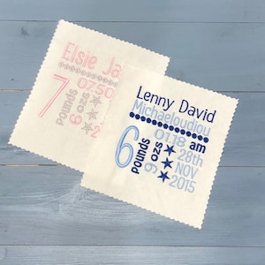 May include: Two white baby blankets with embroidered birth announcements. The top blanket is pink and says "Elsie Ja 7 pounds 6 ozs 07.50". The bottom blanket is blue and says "Lenny David Michaeloudiou 6 pounds 6 ozs 01.18 am 28th NOV 2015".