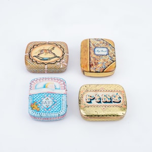 May include: Four vintage rectangular tins with decorative designs. One tin features a rocking horse, another a book with the text "My Book", a third a baby in a crib, and the last one has the word "PINS".