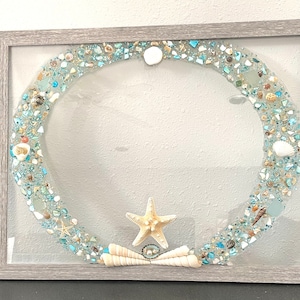 May include: A framed artwork featuring a blue and white seashell wreath with a starfish and seashells in the center.