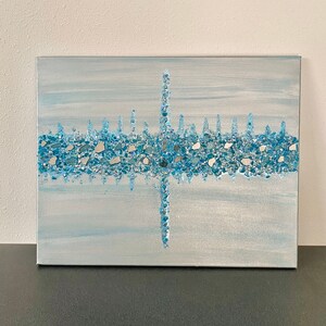 May include: Abstract artwork on canvas featuring a skyline design. The painting uses shades of blue and silver, with a textured, mosaic-like application of small, reflective pieces. The artwork is mounted on a rectangular canvas.