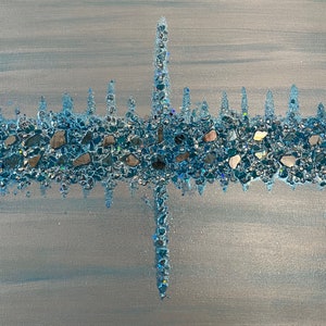 May include: Abstract artwork on canvas featuring a horizontal band of blue and silver stones and glitter. A vertical line of the same materials intersects the horizontal band. The background is a light blue and silver gradient.