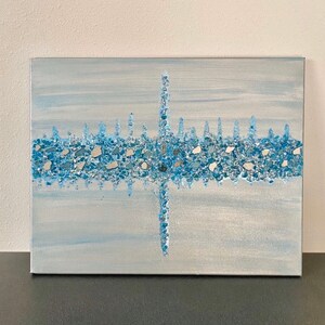 May include: Abstract canvas art featuring a light blue and silver background. A horizontal band of blue and silver glass pieces is centered on the canvas, with a vertical line of glass pieces intersecting it. The artwork has a textured appearance.