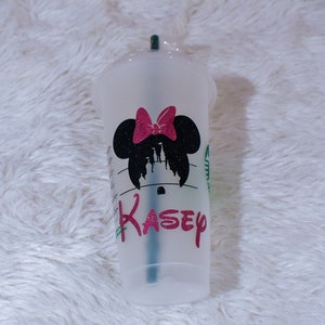 Puede incluir: Un vaso de pl&aacute;stico transparente para bebidas fr&iacute;as con un dise&ntilde;o de silueta de Minnie Mouse negra y un lazo rosa brillante. El nombre "Kasey" est&aacute; impreso en rosa debajo. Una pajita verde es visible dentro.