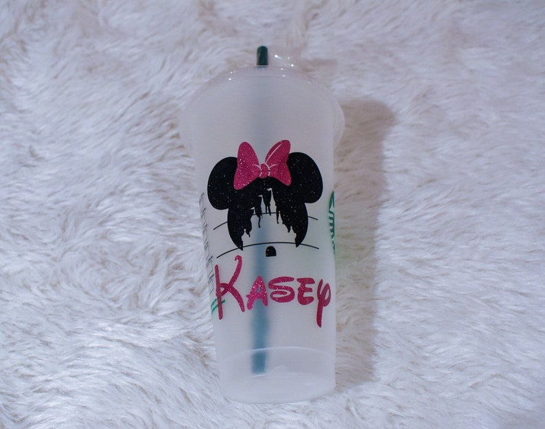 Puede incluir: Un vaso de pl&aacute;stico transparente para bebidas fr&iacute;as con un dise&ntilde;o de silueta de Minnie Mouse negra y un lazo rosa brillante. El nombre "Kasey" est&aacute; impreso en rosa debajo. Una pajita verde es visible dentro.
