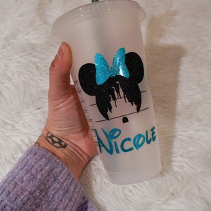 Puede incluir: Un vaso de pl&aacute;stico transparente de Starbucks con un dise&ntilde;o de silueta de Minnie Mouse negra y un lazo turquesa. El nombre "Nicole" est&aacute; escrito en gui&oacute;n turquesa. El vaso est&aacute; sostenido por una persona.