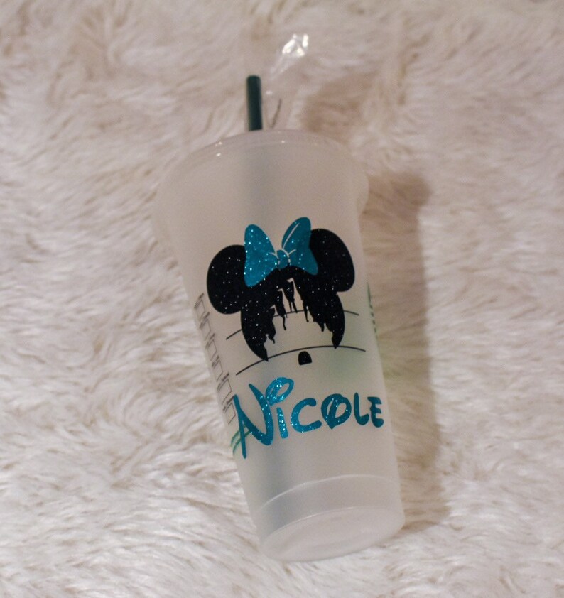 Puede incluir: Un vaso de pl&aacute;stico transparente con una pajita verde azulado. El vaso presenta una silueta negra de Minnie Mouse con un lazo verde azulado y el nombre "Nicole" en letras brillantes verde azulado. La taza tiene un logotipo de Starbucks.