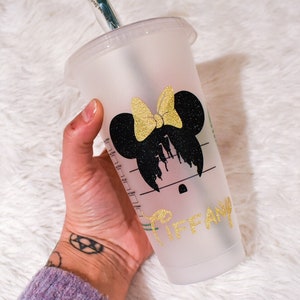 Puede incluir: Un vaso de pl&aacute;stico transparente para bebidas fr&iacute;as con tapa y pajita. El vaso presenta una silueta negra de Minnie Mouse con un lazo dorado brillante y el nombre "Tiffany" en letras doradas brillantes.