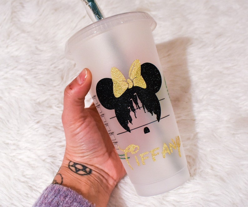 Puede incluir: Un vaso de pl&aacute;stico transparente para bebidas fr&iacute;as con tapa y pajita. El vaso presenta una silueta negra de Minnie Mouse con un lazo dorado brillante y el nombre "Tiffany" en letras doradas brillantes.